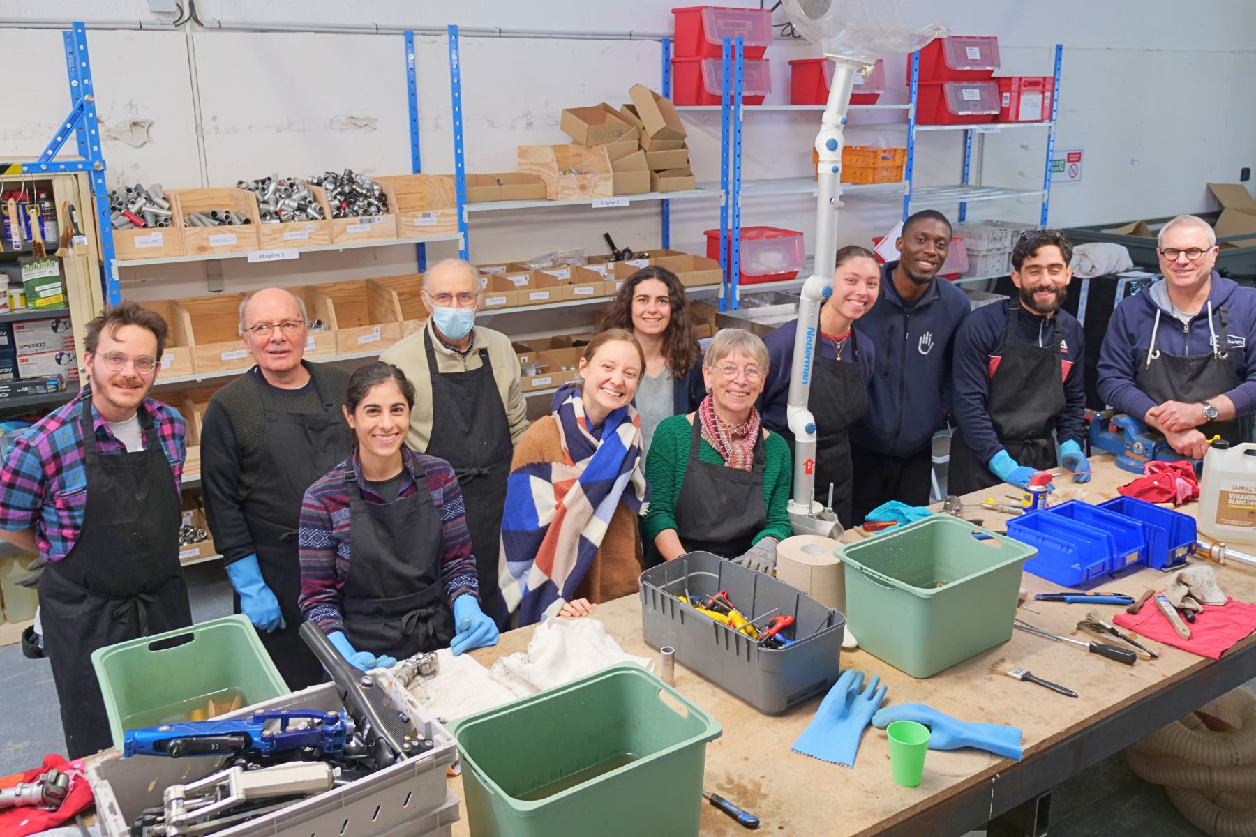 In unserer Recycling-Werkstadt in der Nähe von Lyon. Ein Gruppenfoto des Teams bei der Arbeit. Alle lächeln breit in die Kamera.